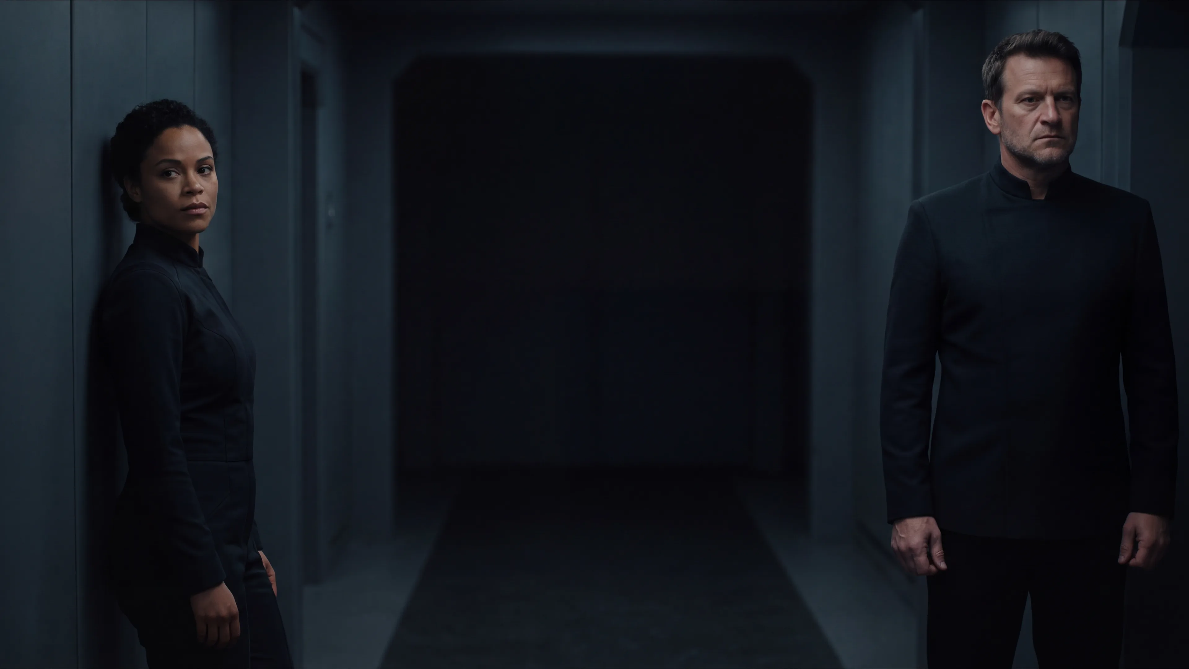 Two human officers standing a pace apart at either end of a dim starship corridor, neither one closing the distance